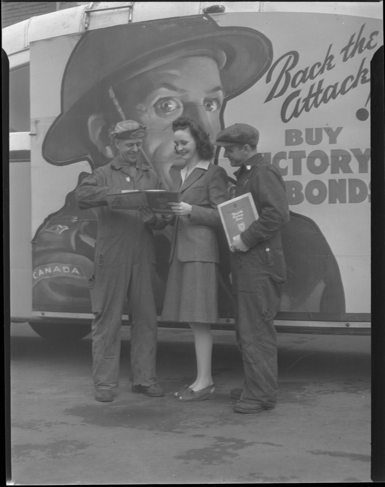 Two shipyard workers and a woman reading a booklet together in Toronto, around 1945